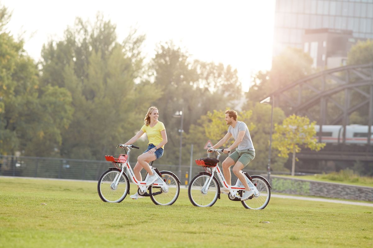 Woman and man riding Call a Bike bicycles through a park